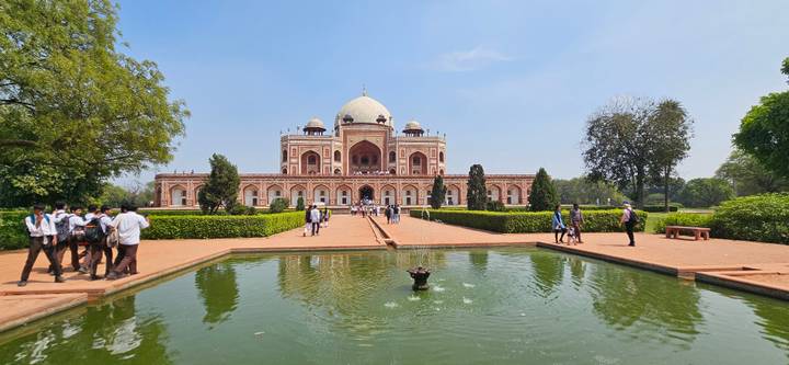 Wide view of Humayun’s Tomb reflected in a tranquil pool, framed by manicured gardens and blue skies.