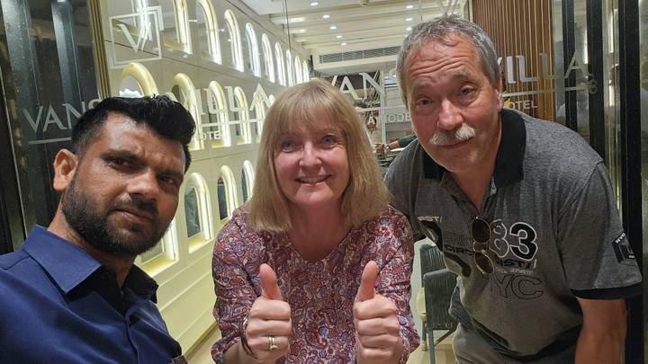 Guide and two travelers give thumbs up inside a stylish hotel lobby with mirrored walls.
