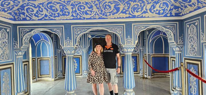 Couple stand inside a vivid blue-painted room with ornate arches and white floral motifs.