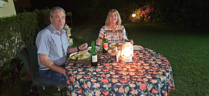 Couple enjoy an outdoor candlelit dinner on a lawn at night with patterned tablecloth.