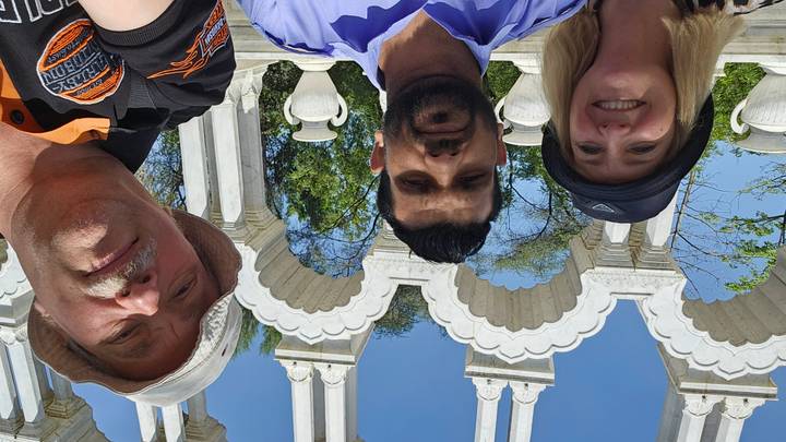 Selfie of guide and two travelers beneath white ornamental arches on a sunny day.