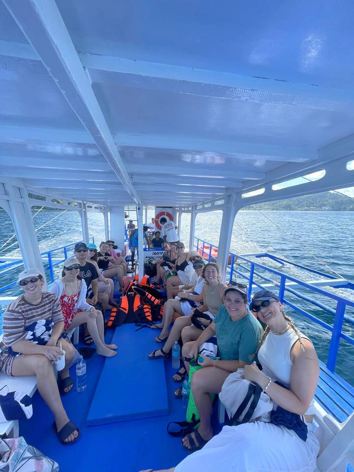 Large group of travelers seated aboard an open boat cruising over deep blue tropical waters.