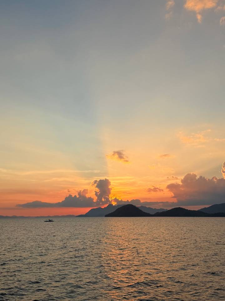 Vibrant sunset sky with orange and pink hues over distant island silhouettes and calm sea.