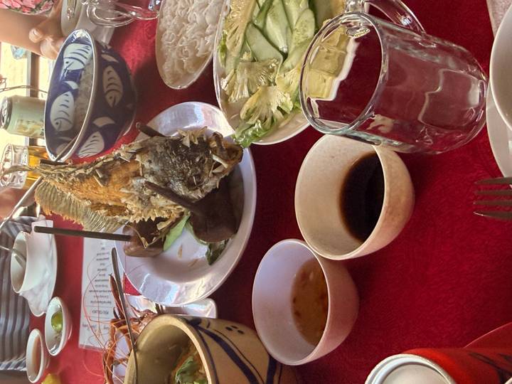 Close-up of a whole fried fish and Vietnamese side dishes laid out on a red tablecloth.