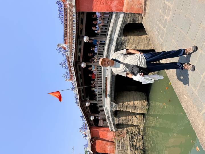 Tourist poses in front of Hoi An's historic Japanese Covered Bridge over a green canal.