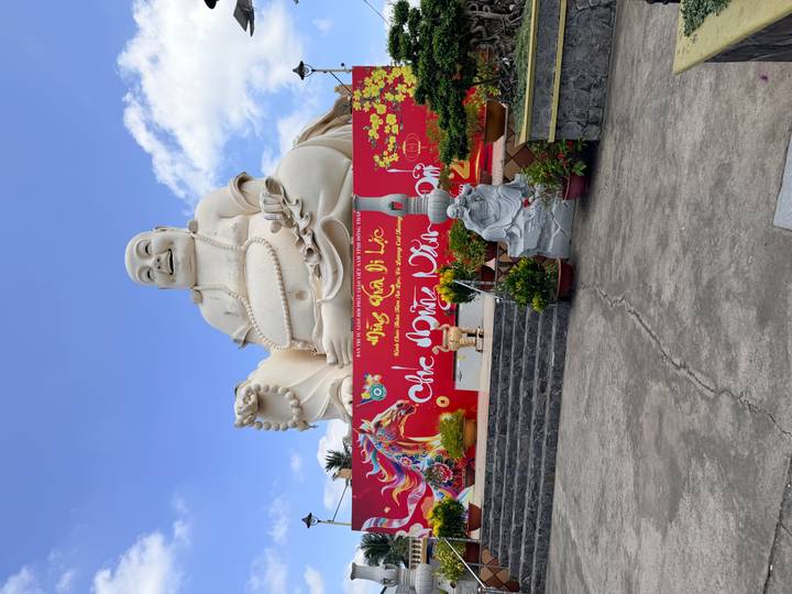 Gigantic white Laughing Buddha statue sits above a colourful mural and courtyard.