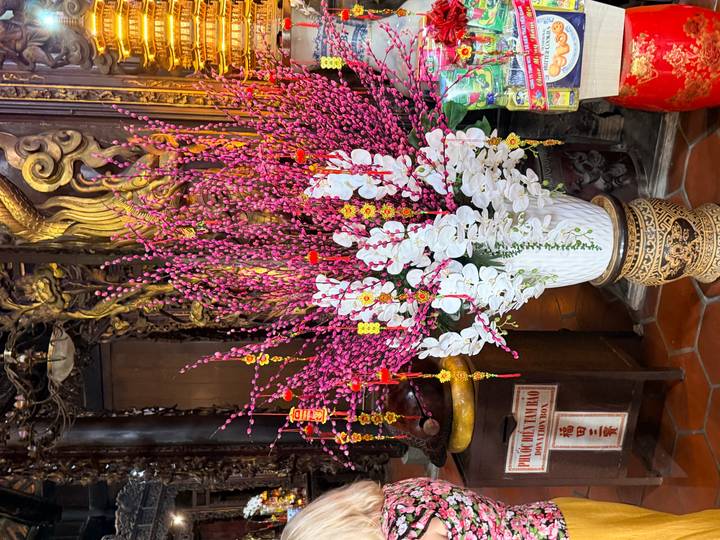 Decorative arrangement of pink and white blossoms inside an ornate Vietnamese temple.