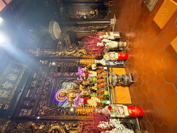 Dimly lit temple interior with golden Buddha statue, offerings and ornate wood carvings.