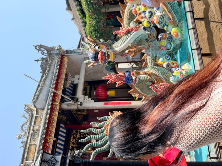 Colorful ceramic dragon statues in a temple courtyard partly blocked by a visitor’s hair.