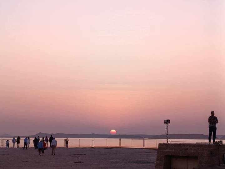 Soft pink sunset over a broad river as cruise passengers watch from deck.