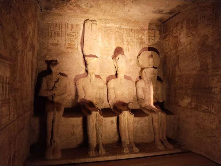 Dimly lit interior of Abu Simbel shows four seated pharaonic statues carved from stone.