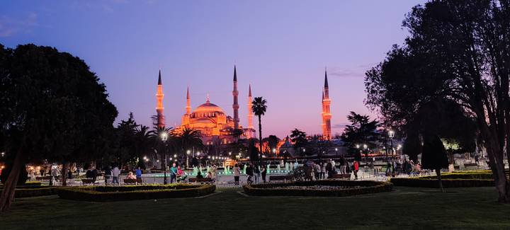 Blue Mosque illuminated at dusk with fountains and visitors enjoying the landscaped square.