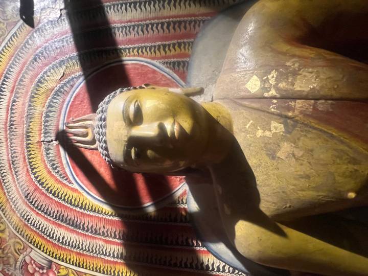 Dimly lit golden Buddha statue inside a cave temple with painted ceiling.