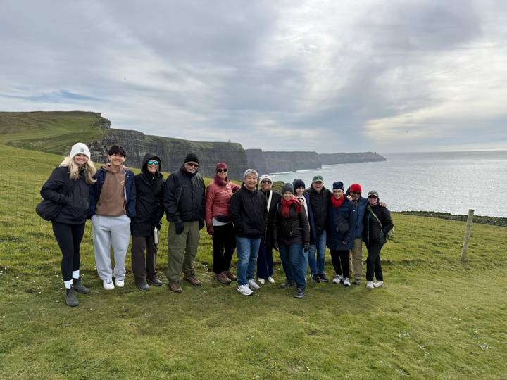 Travel group poses on grassy cliff edge with the Cliffs of Moher behind.