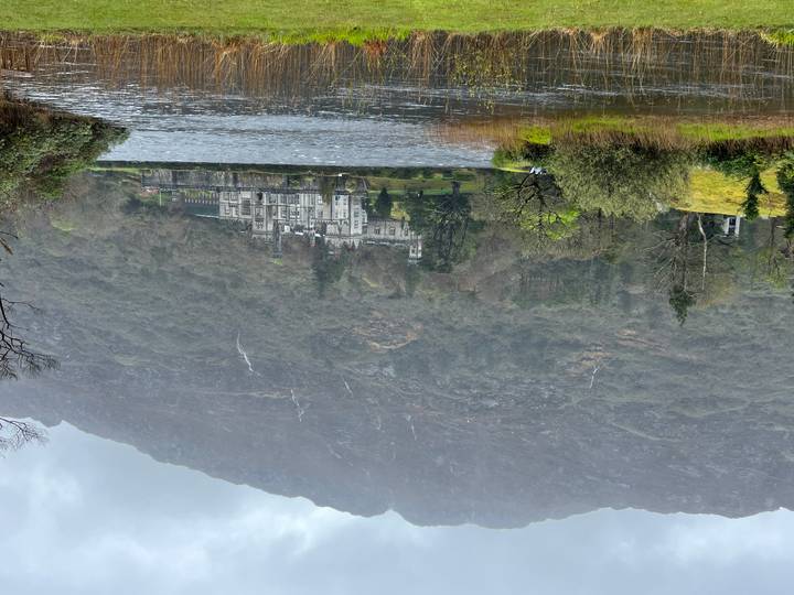 Historic stone abbey sits lakeside beneath misty mountains and waterfalls.
