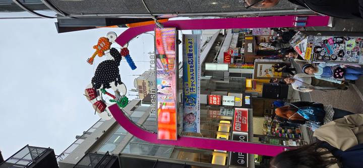 Colorful archway marks Takeshita Street bustling with shoppers and signs.