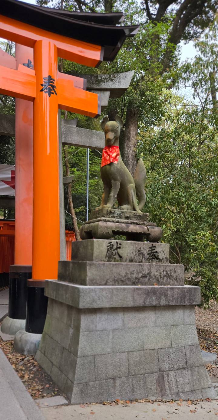 Stone fox statue wearing red bib at Fushimi Inari shrine gate.