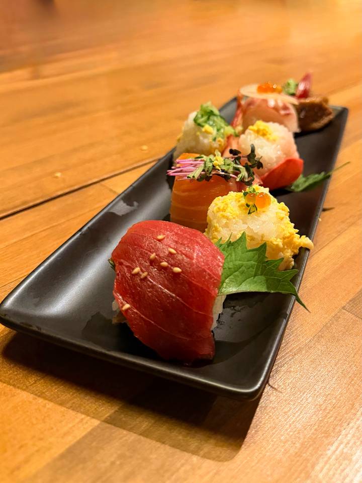 An elegant plate of assorted nigiri sushi on a dark ceramic dish.
