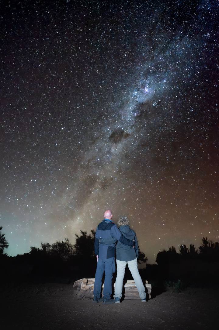 Two stargazers admire the Milky Way glittering across a clear desert night sky.