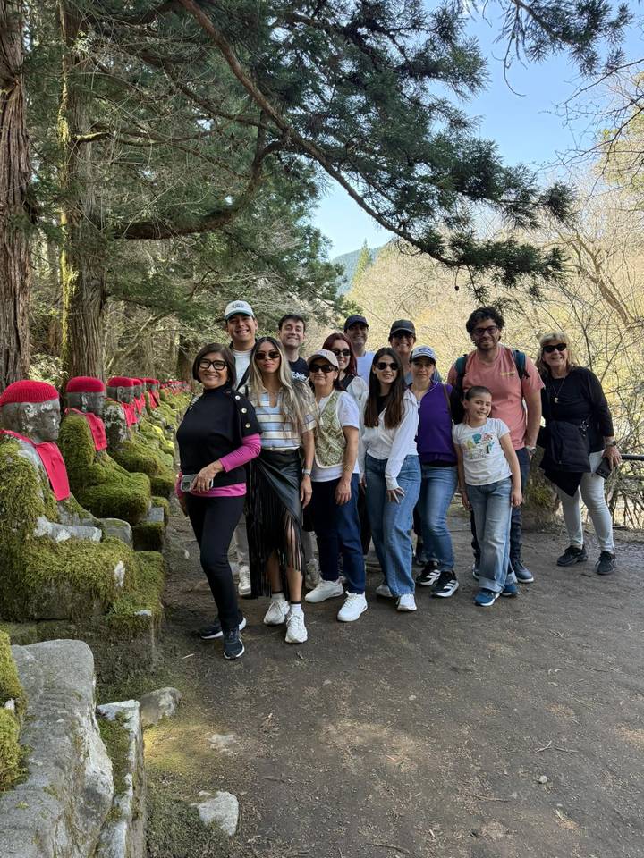 Tour group standing beside moss-covered stone statues along a forest trail.