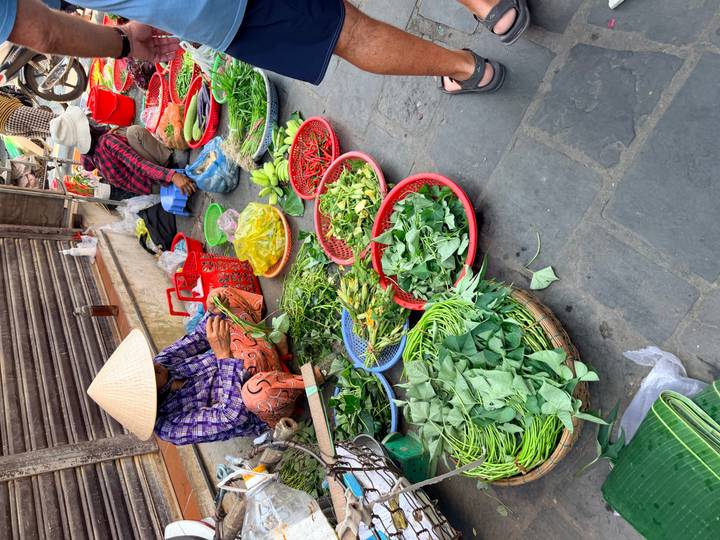 Local market stall with vendor in conical hat selling baskets of fresh green vegetables and chilies