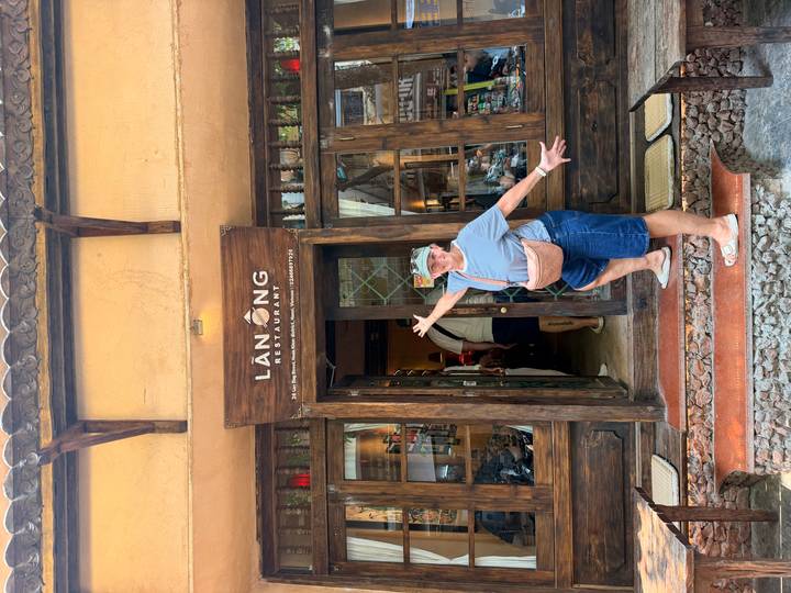 Traveler enthusiastically gesturing at the entrance of a rustic wooden restaurant