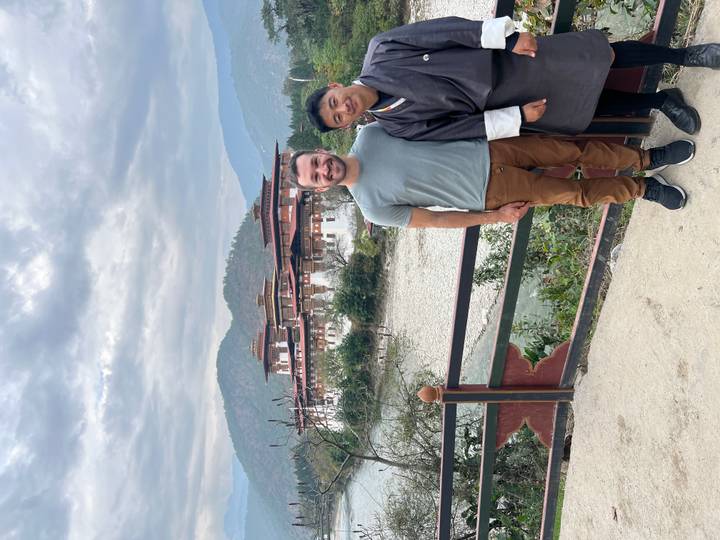 Two travellers posing in front of Punakha Dzong beside river under cloudy sky
