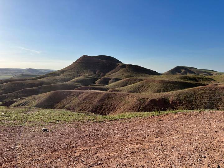 Rugged reddish hills and valleys under a clear blue sky in a semi-arid landscape.