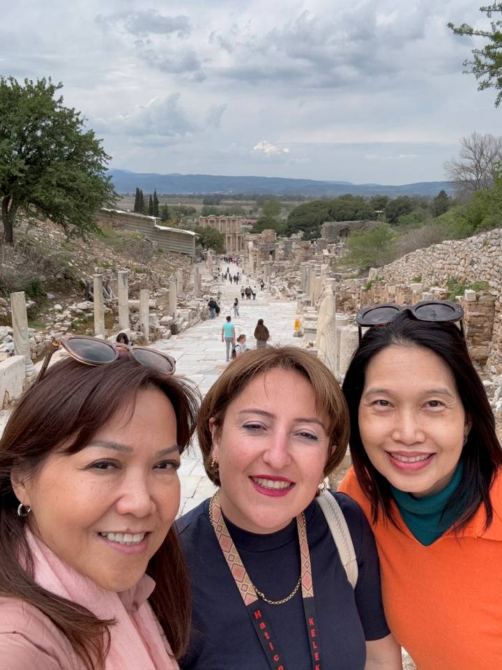 Close-up selfie of three women with the marble avenue of ancient Ephesus stretching behind them.