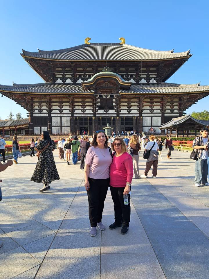 Visitors gathered in front of the wooden Todai-ji temple hall with landscaped grounds and blue skies.