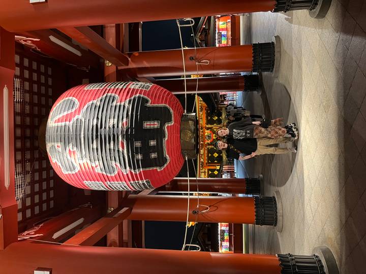Couple standing beneath giant red lantern at Senso-ji Temple gate illuminated at night.