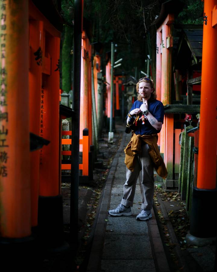 Traveler framed by vivid orange torii gates along pathway at Fushimi Inari Shrine.