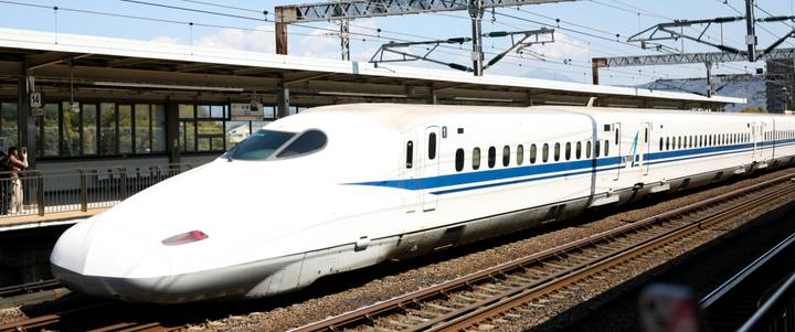 White Shinkansen bullet train waiting on tracks at a Japanese station.