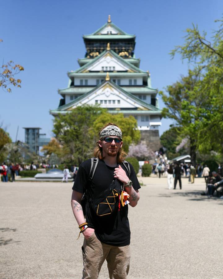 Traveler wearing bandana standing in front of Osaka Castle on a sunny spring day.
