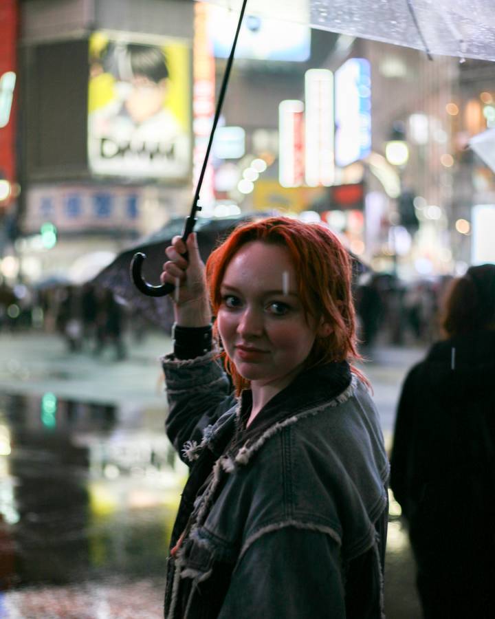 Nighttime street scene with woman holding umbrella at illuminated Shibuya Crossing.