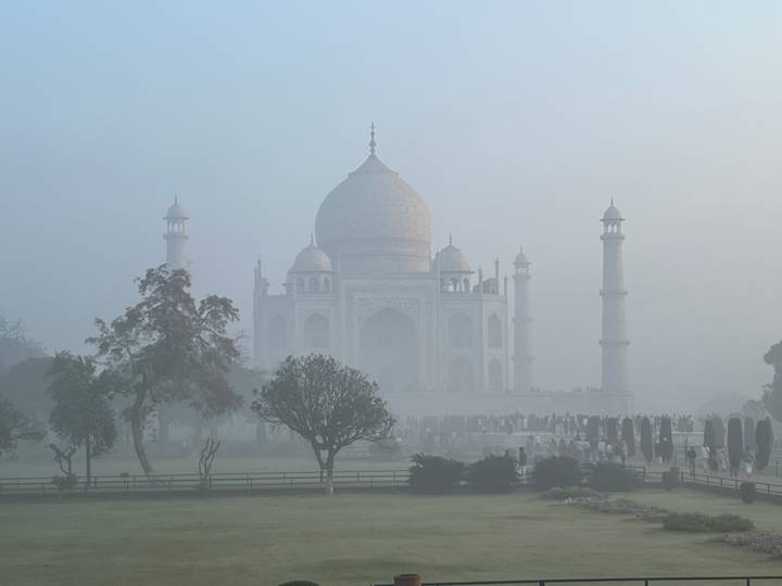 Taj Mahal shrouded in thick morning fog with silhouettes of visitors and trees.