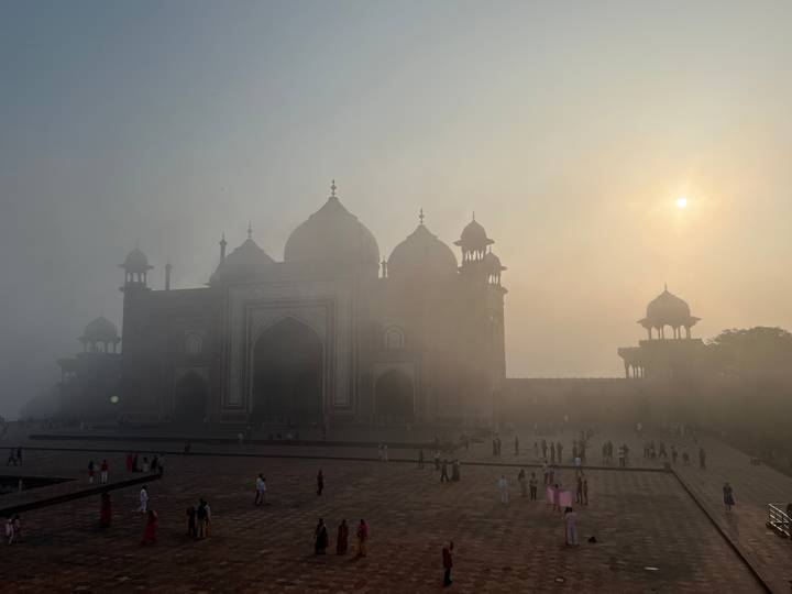 Silhouetted mosque building of Taj complex emerging from sunrise haze with soft sun disc.