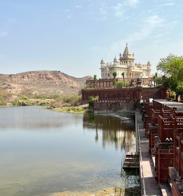 Marble memorial Jaswant Thada by tranquil lake with arid hills in background.