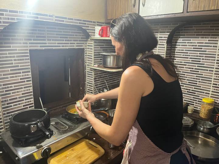 Traveler participates in a home-style cooking class, stirring spices on a small kitchen stove.