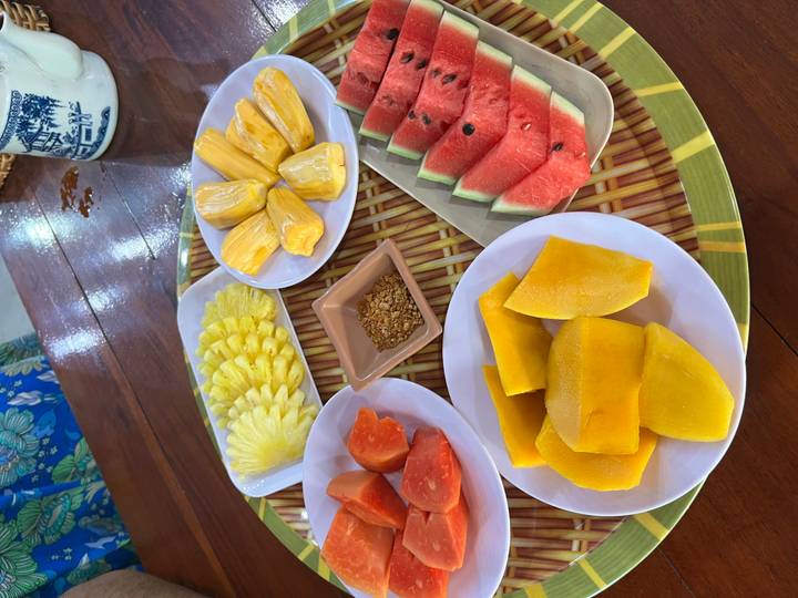 Colorful platter of sliced tropical fruits including mango, papaya, pineapple and watermelon on a bamboo tray.
