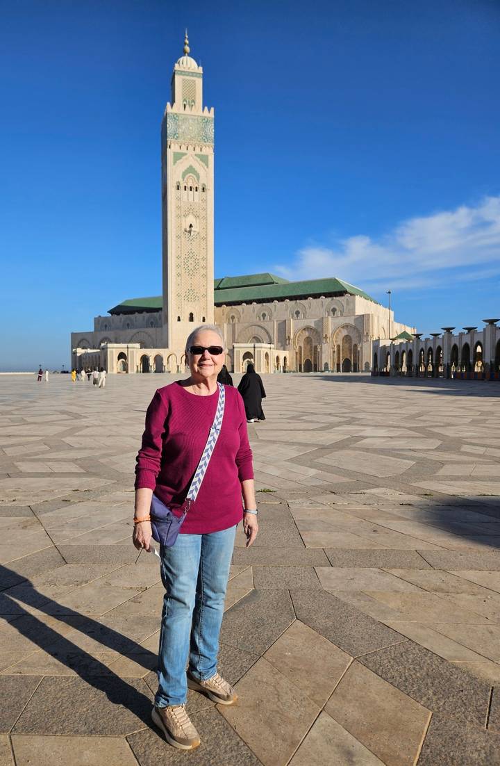 Smiling traveler standing on the vast courtyard of Hassan II Mosque with towering minaret behind.