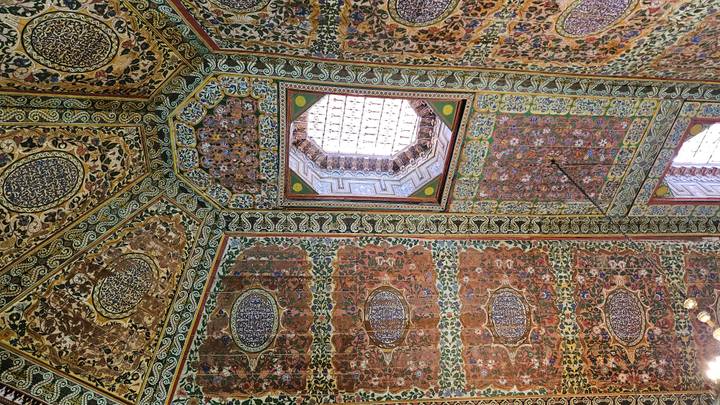Highly ornamented Moroccan ceiling with colorful geometric and floral patterns around a skylight.