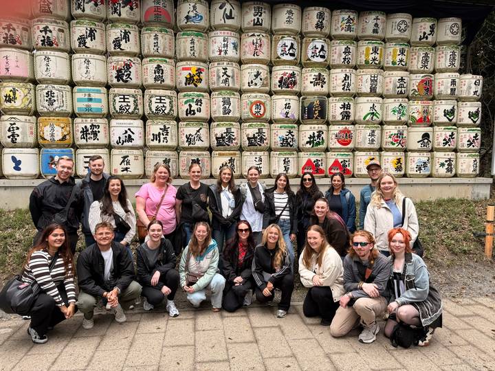 Travelers stand before rows of decorative sake barrels at Meiji Shrine.