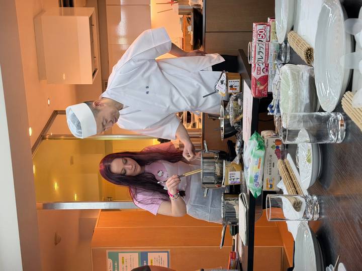 Student and sushi chef stir ingredients together at a countertop during lesson.