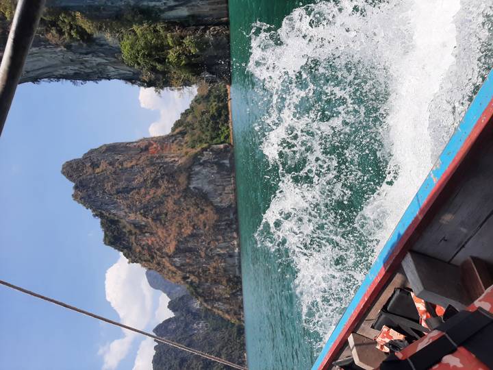 Action shot from a long-tail boat with water splashing up toward dramatic limestone cliffs in Khao Sok lake.