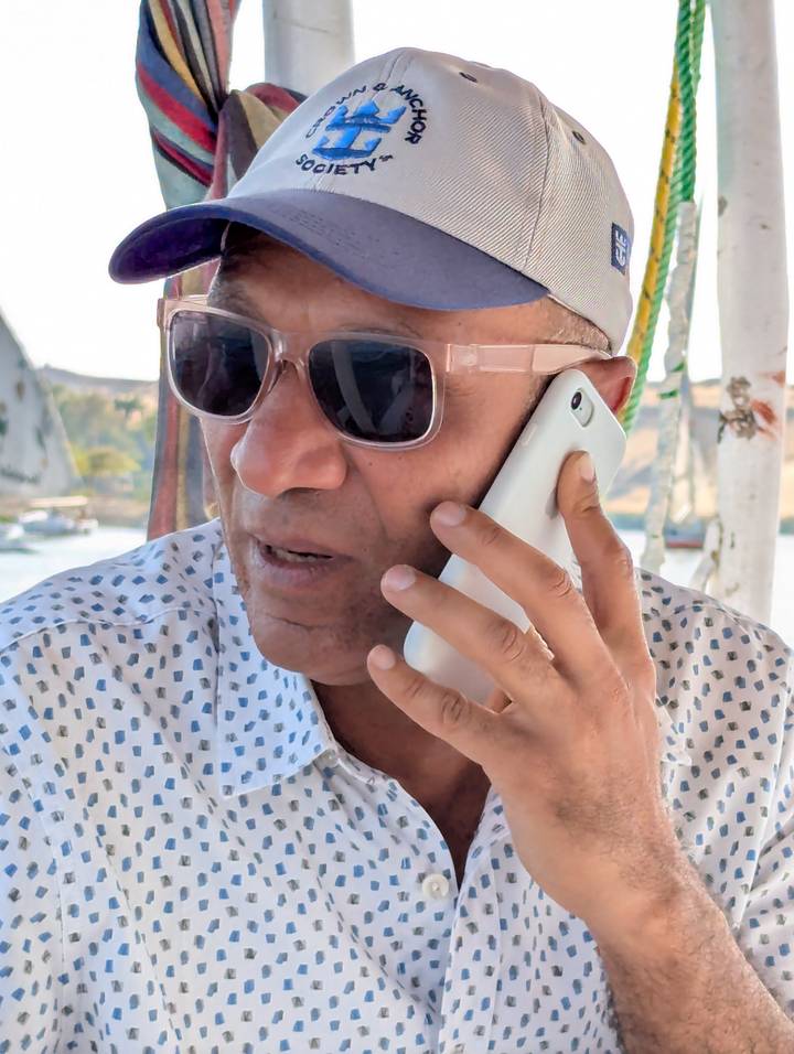 Close-up portrait of a man wearing sunglasses talking on a smartphone aboard a boat on the Nile.