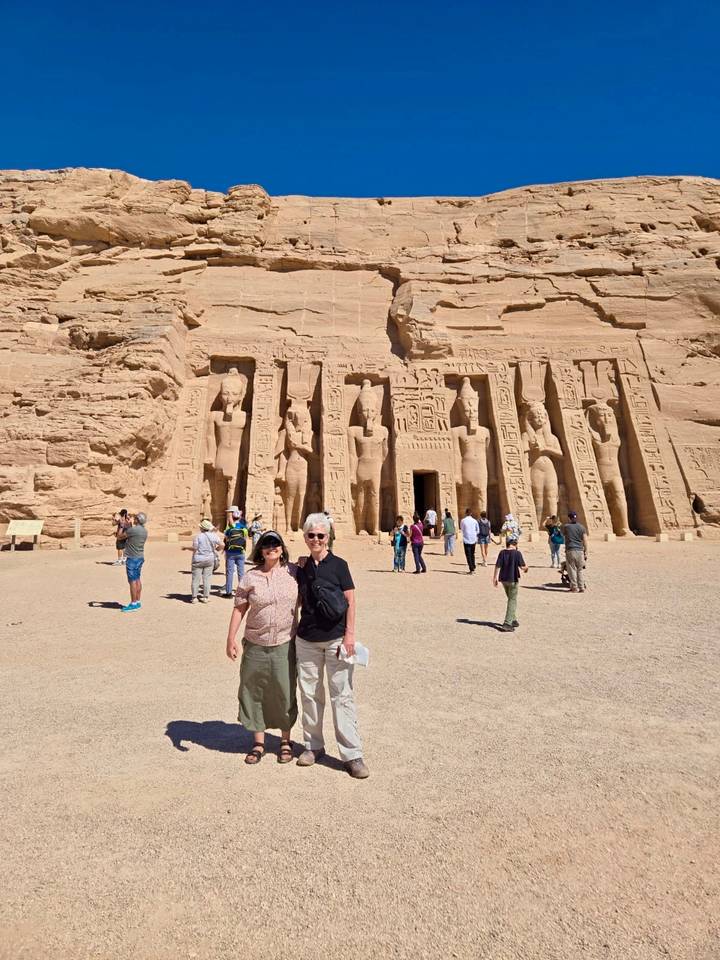 Tourists gather before the colossal statues of Abu Simbel temple under bright desert sun.