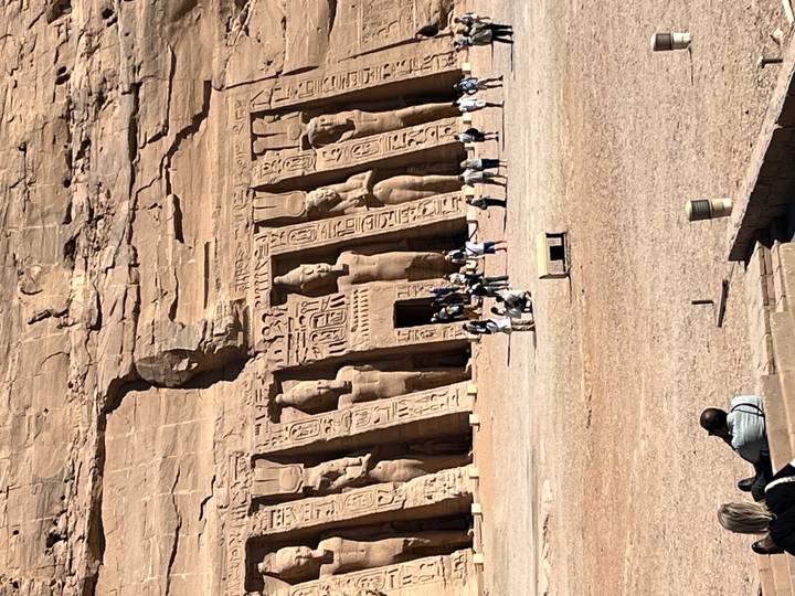 Wide shot of Abu Simbel’s façade with numerous tourists exploring the sandy forecourt.