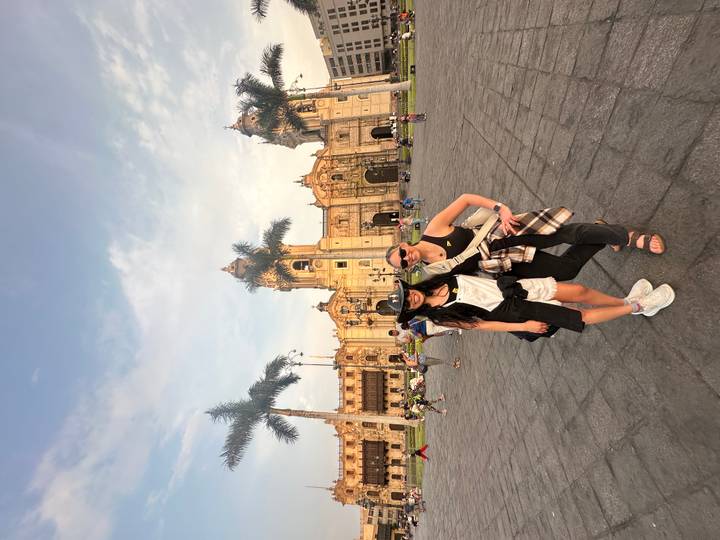 Two travellers pose in Lima’s Plaza Mayor with the ornate colonial cathedral in warm evening light.