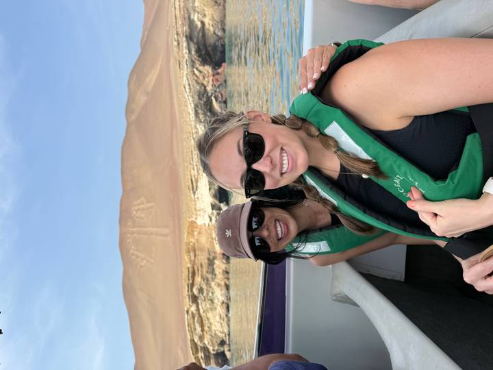 Smiling friends on a boat with the Paracas Candelabra geoglyph etched into the desert hill behind.